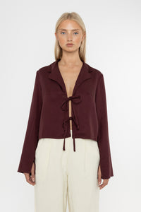 Woman wearing a burgundy brown jacket and white trousers on a white background