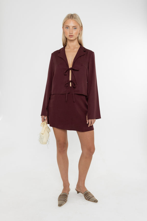 Woman wearing a burgundy brown jacket and mini skirt with mules on a white background