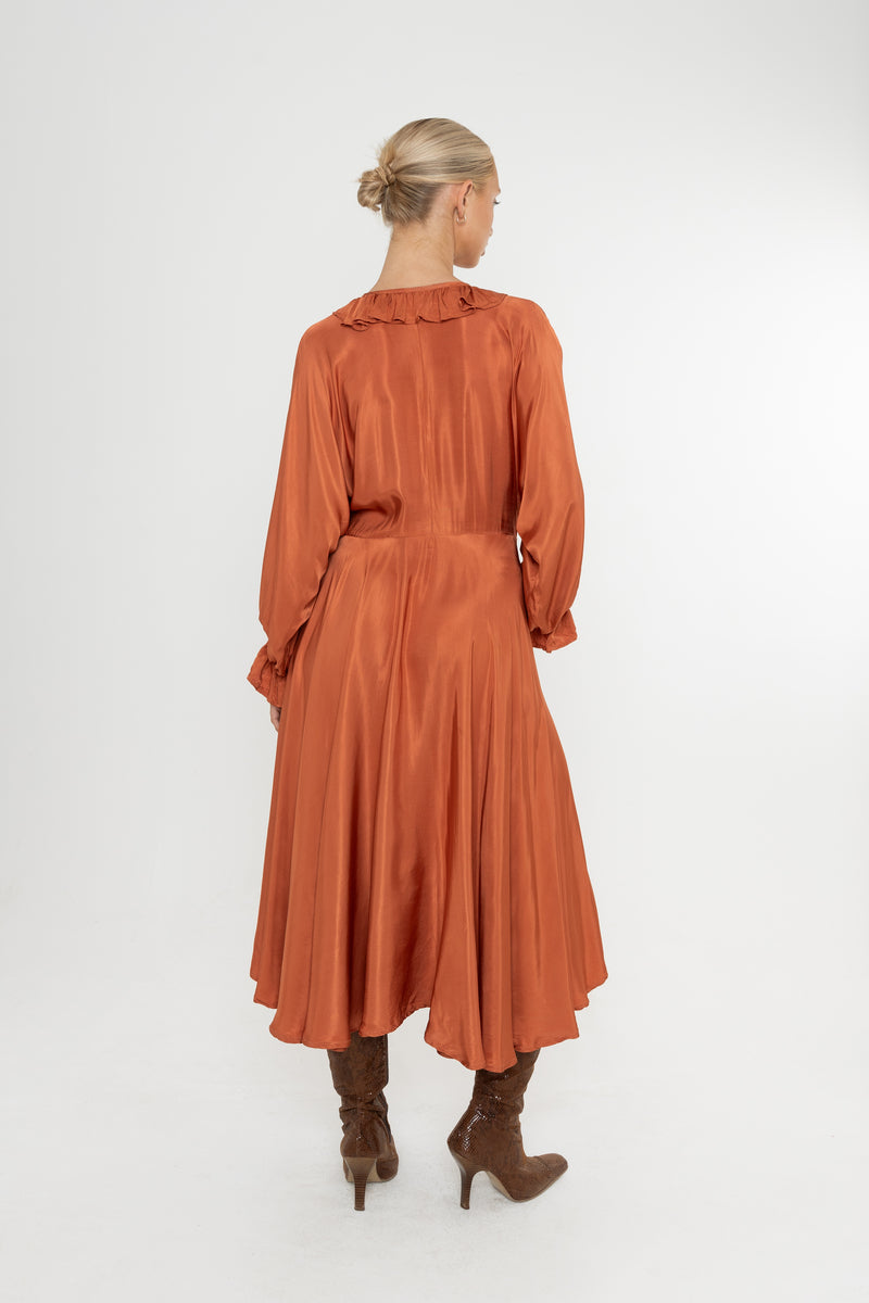 Woman wearing a rust-colored satin dress with long sleeves  and a ruffle collar with brown boots on a white background