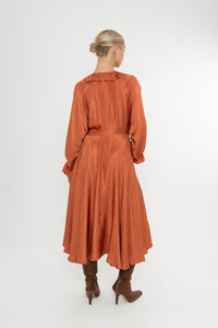 Woman wearing a rust-colored satin dress with long sleeves  and a ruffle collar with brown boots on a white background