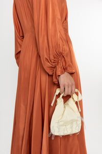 Woman wearing a rust-colored satin dress with long sleeves  and a ruffle collar with a yellow bag on a white background