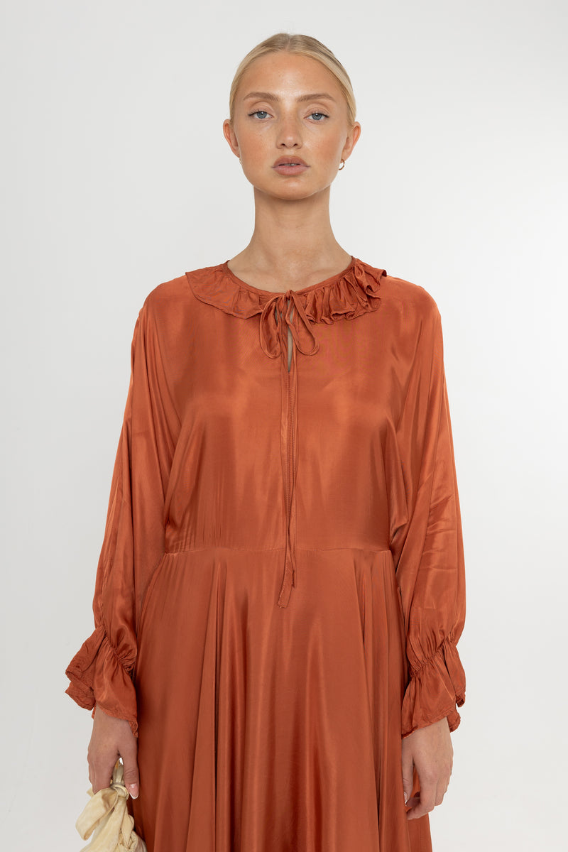 Woman wearing a rust-colored satin dress with long sleeves  and a ruffle collar on a white background