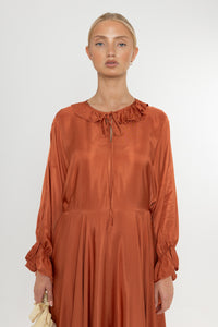 Woman wearing a rust-colored satin dress with long sleeves  and a ruffle collar on a white background