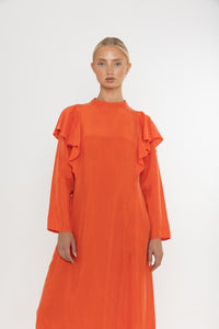 Woman wearing an orange vermillion red dress with ruffled long sleeves on a white background