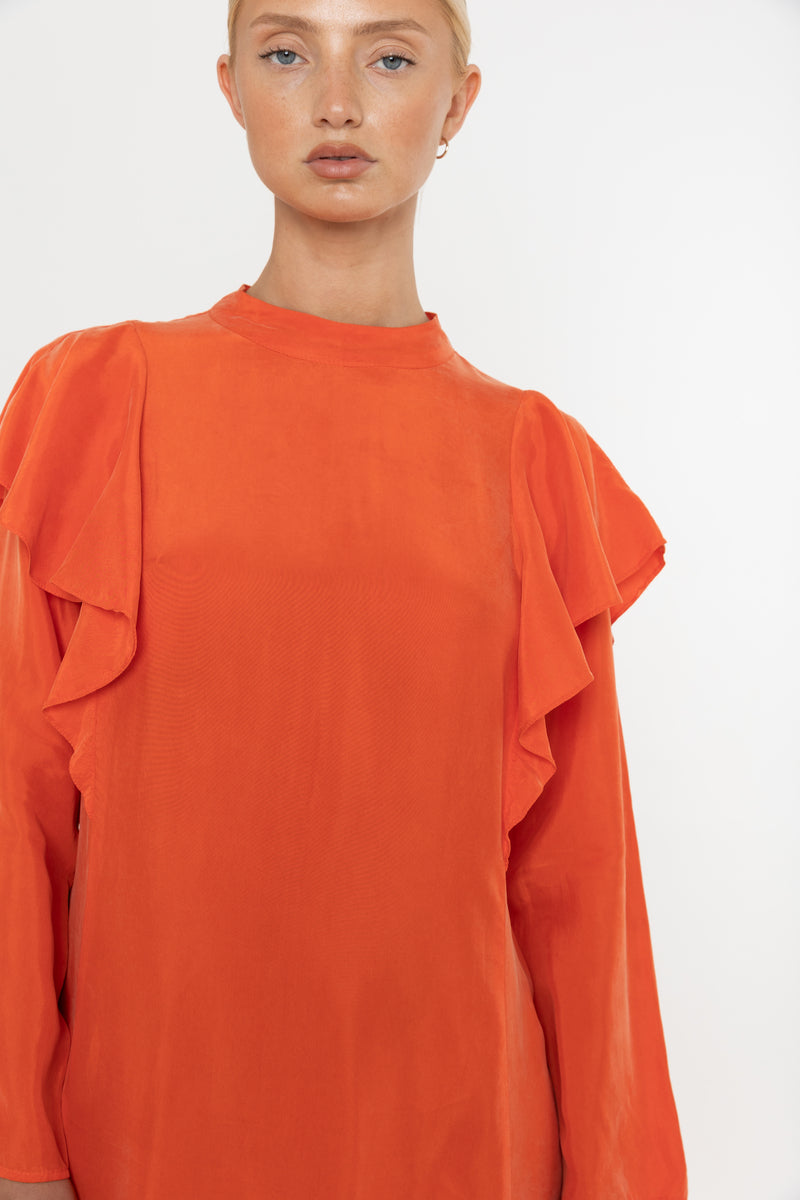 Woman wearing an orange vermillion red dress with ruffled long sleeves on a white background