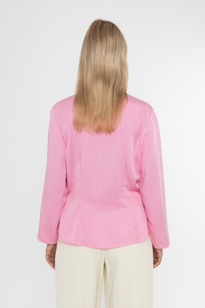 Woman wearing a Deidei Malala pink blazer jacket and white trousers on a white background