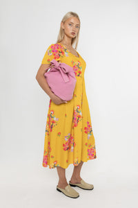 Woman wearing a Deidei Maya midi dress in a yellow floral print holding a pink bag on a white background