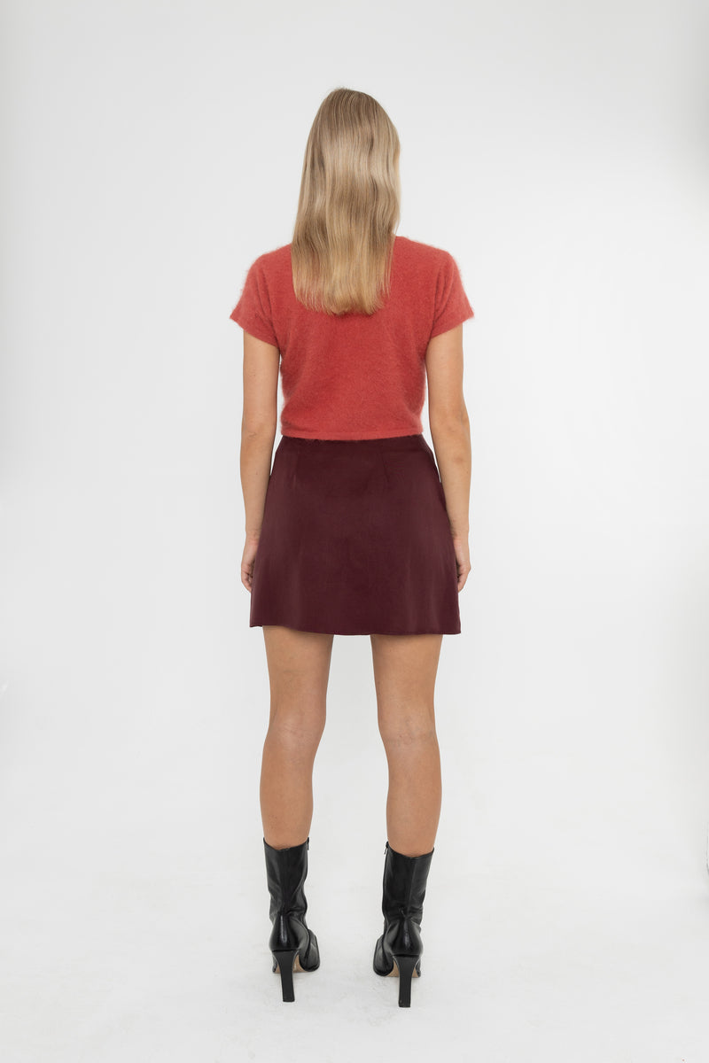 Woman wearing a red crop jumper and Deidei Noor burgundy brown skirt with black boots on a white background