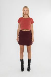 Woman wearing a red crop jumper and Deidei Noor burgundy brown skirt with black boots on a white background
