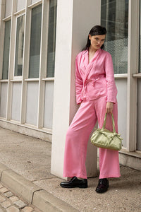 Person in a pink outfit standing against a building with large windows.