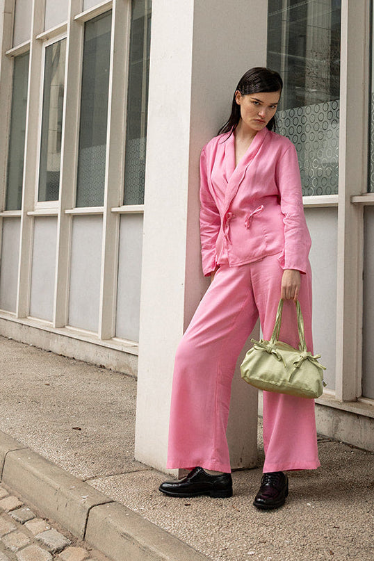 Person in a pink outfit standing against a building with large windows.