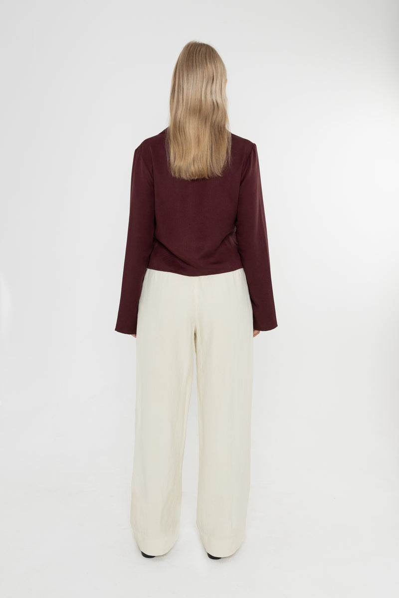 Woman wearing a burgundy brown jacket and white trousers with snake print loafers on a white background