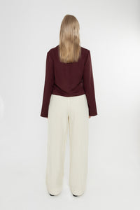 Woman wearing a burgundy brown jacket and white trousers with snake print loafers on a white background