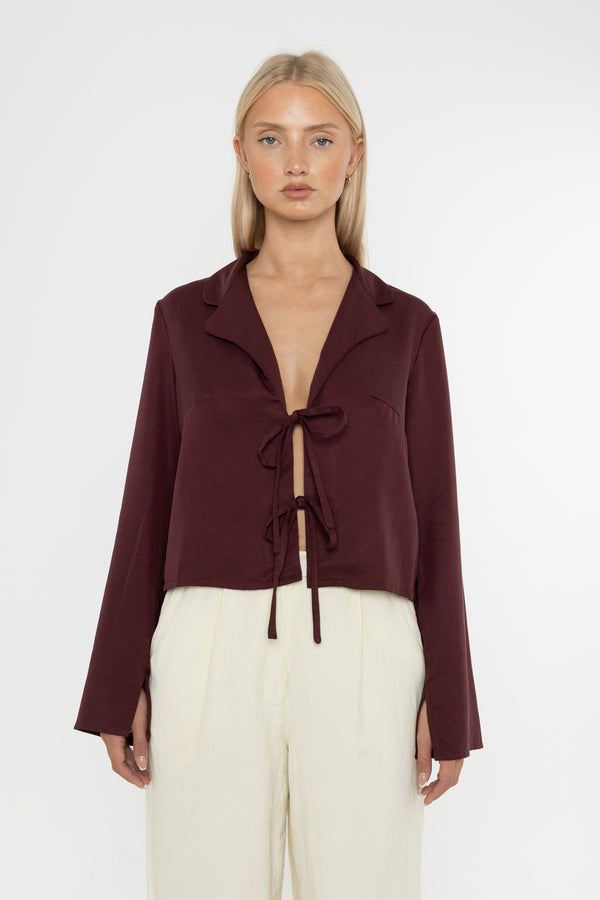 Woman wearing a burgundy brown jacket and white trousers on a white background