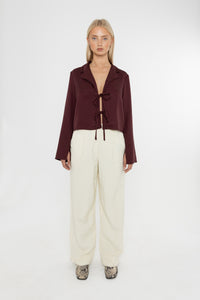 Woman wearing a burgundy brown jacket and white trousers with snake print loafers on a white background
