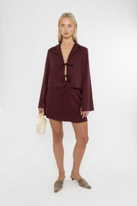 Woman wearing a burgundy brown jacket and mini skirt with mules on a white background