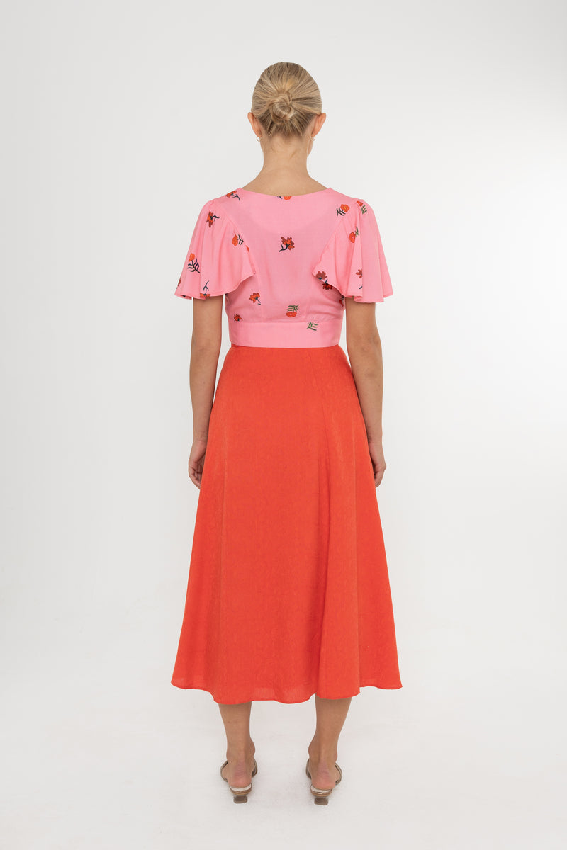 Woman wearing a Deidei Beatrix top with  a pink floral rose print and a red skirt on a white background