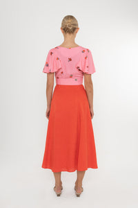 Woman wearing a Deidei Beatrix top with  a pink floral rose print and a red skirt on a white background
