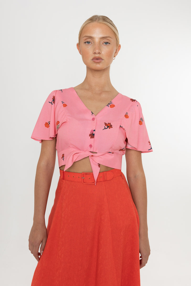 Woman wearing a Deidei Beatrix top with  a pink floral rose print and a red skirt on a white background