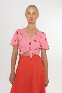 Woman wearing a Deidei Beatrix top with  a pink floral rose print and a red skirt on a white background