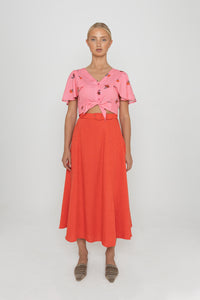 Woman wearing a Deidei Beatrix top with  a pink floral rose print and a red skirt on a white background