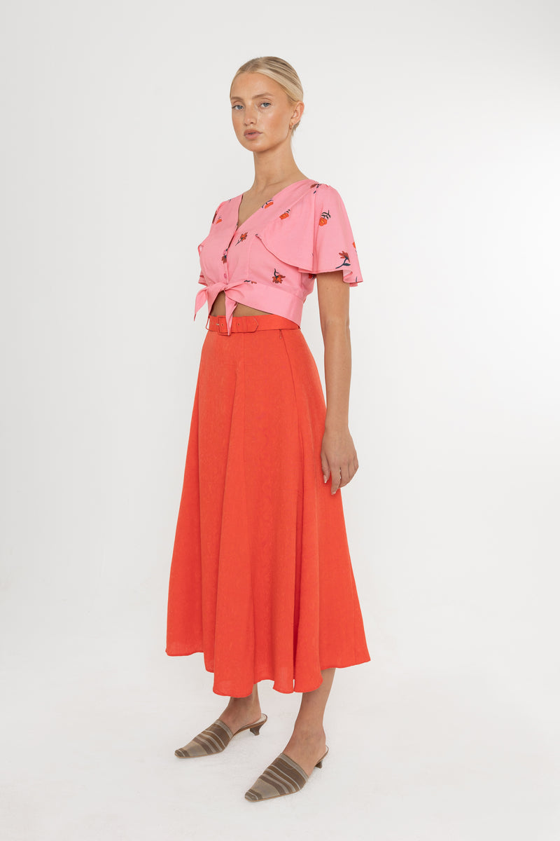 Woman wearing a Deidei Beatrix top with  a pink floral rose print and a red skirt on a white background