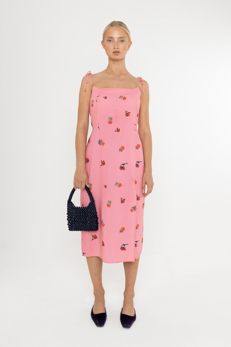 Woman wearing a Deidei Emmeline midi slip dress with pink floral rose print holding a blue vintage bag