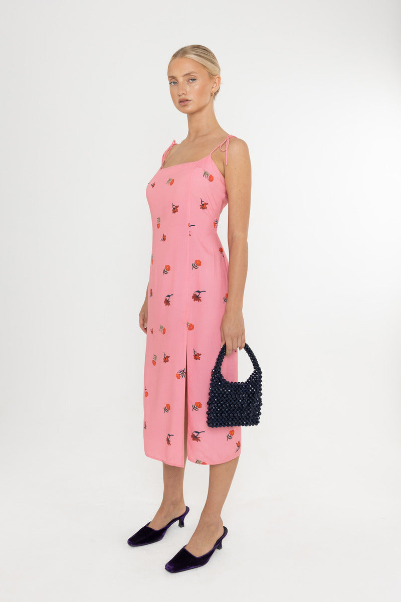 Woman wearing a Deidei Emmeline midi slip dress with pink floral rose print holding a blue vintage bag on a white background