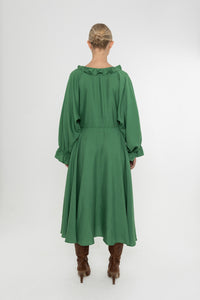 Woman wearing a green Deidei Florence dress with long sleeves and a ruffle collar with brown boots on a white background