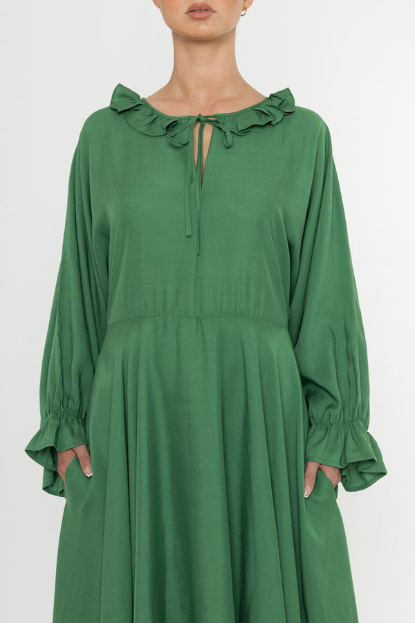 Woman wearing a green Deidei Florence dress with long sleeves and a ruffle collar on a white background