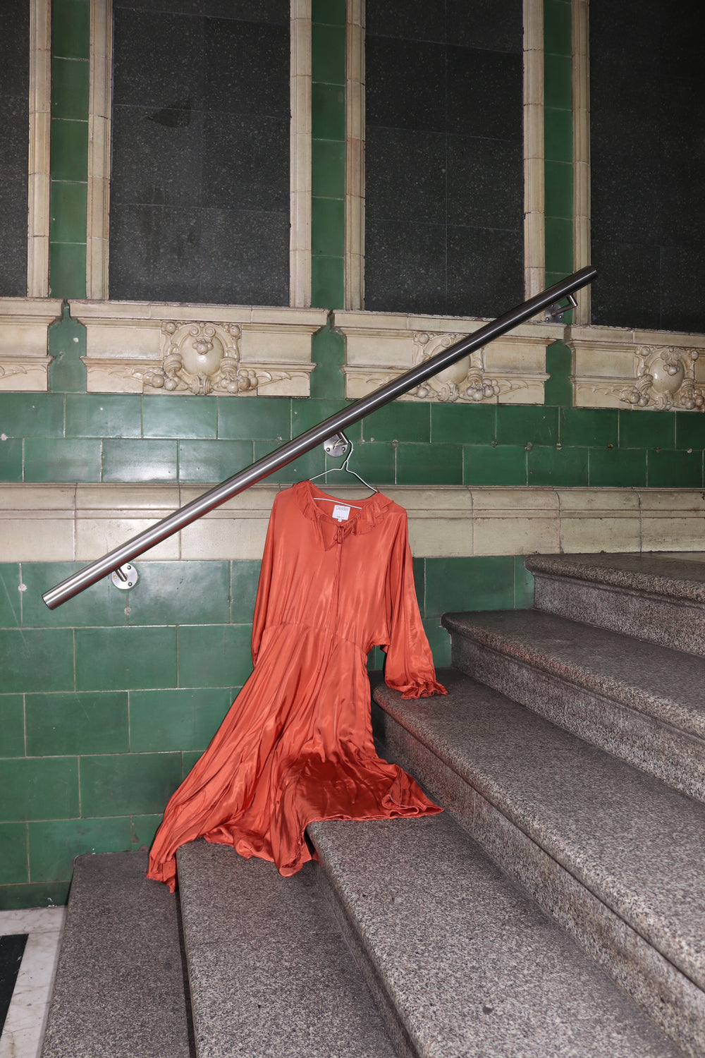 Orange dress draped over a metal rod against a green tiled wall.
