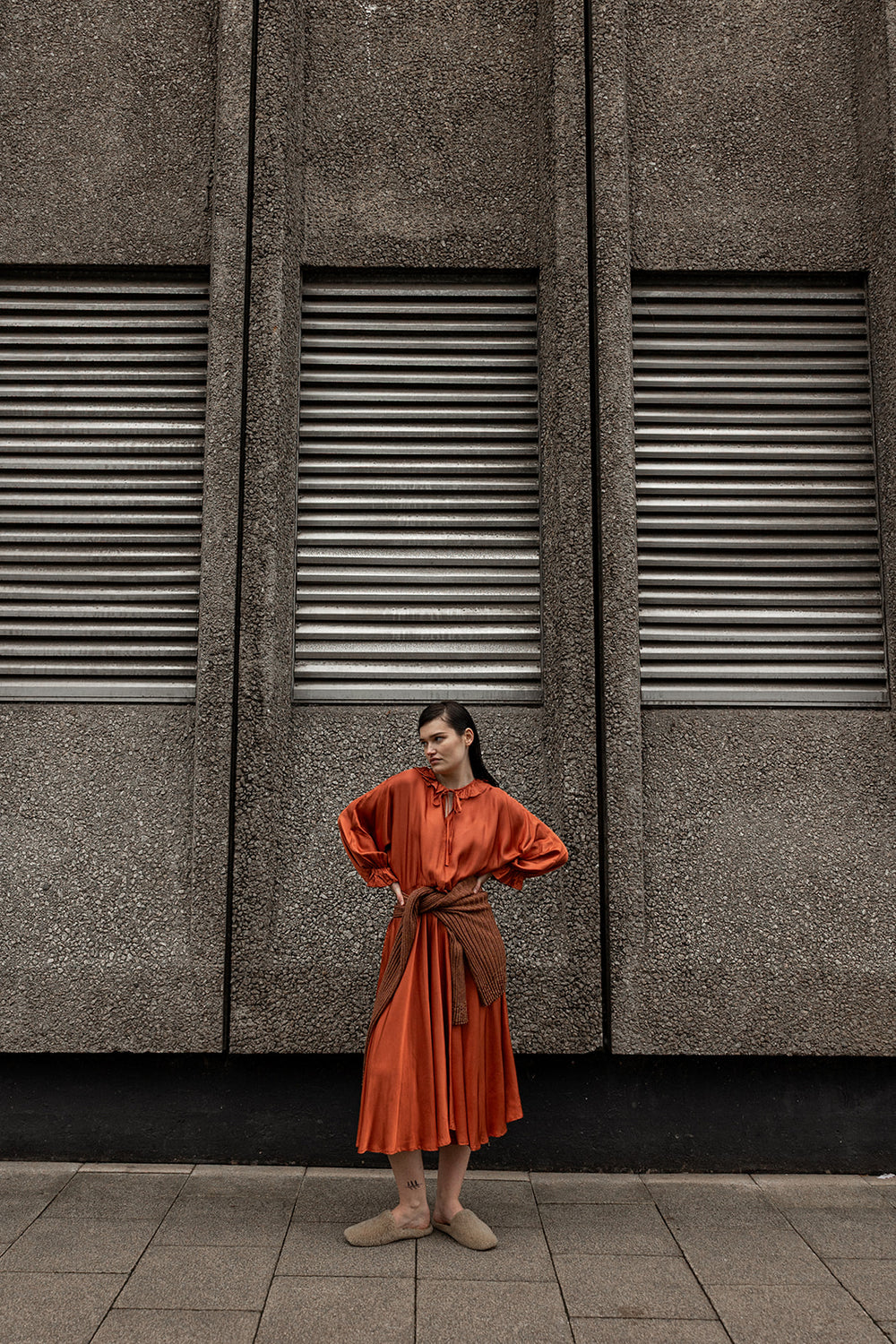 Woman in an orange dress standing against a textured wall with horizontal slats.