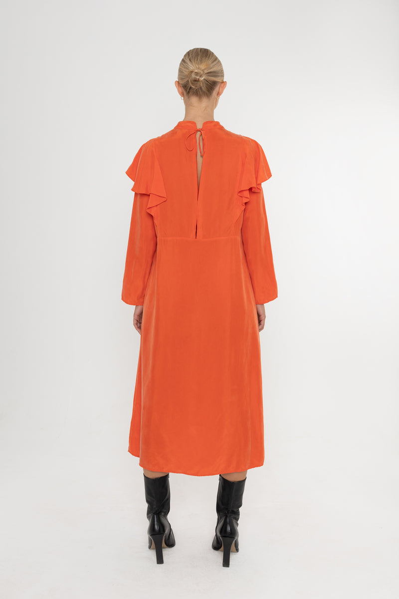 Woman wearing an orange vermillion red dress with ruffled long sleeves and black boots on a white background