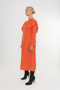 Woman wearing an orange vermillion red dress with ruffled long sleeves and black boots on a white background