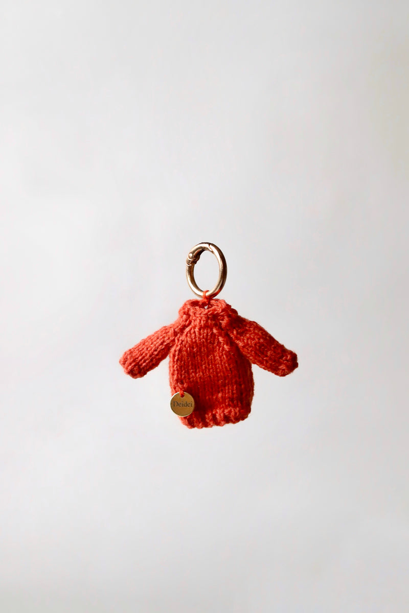 Orange hand knitted bag charm with a Deidei medallian on a white background