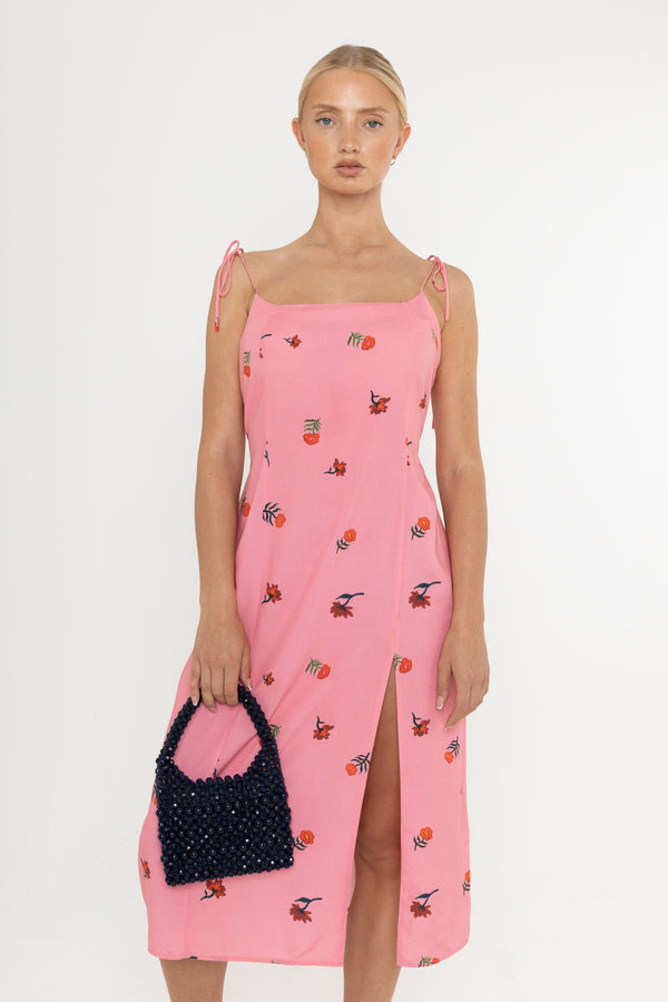 woman wearing pink midi floral dress with a leg slit. Holding a handbag in her right hand. 